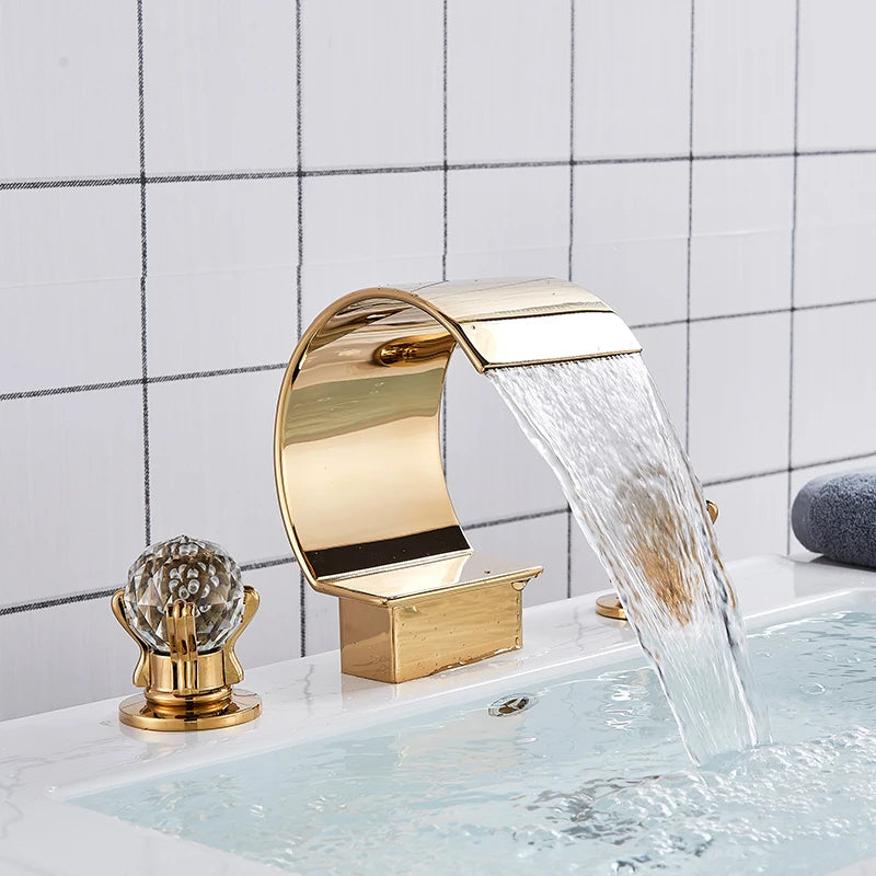 Gold widespread bathroom faucet with waterfall spout and clear crystal-style handles running water