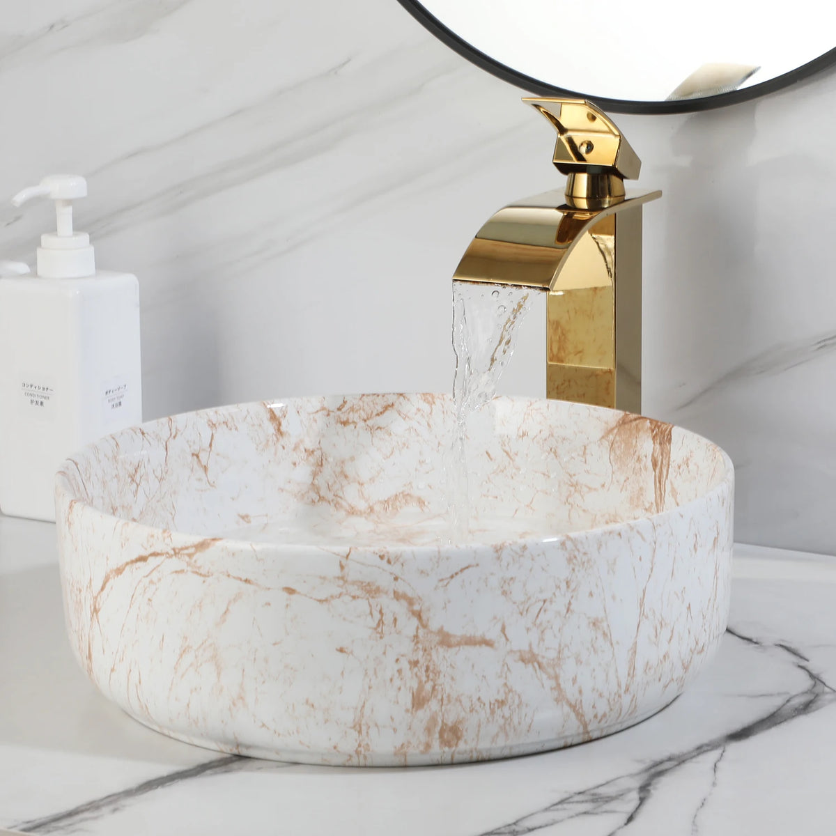 White marble-look vessel sink with gold waterfall faucet under a round mirror