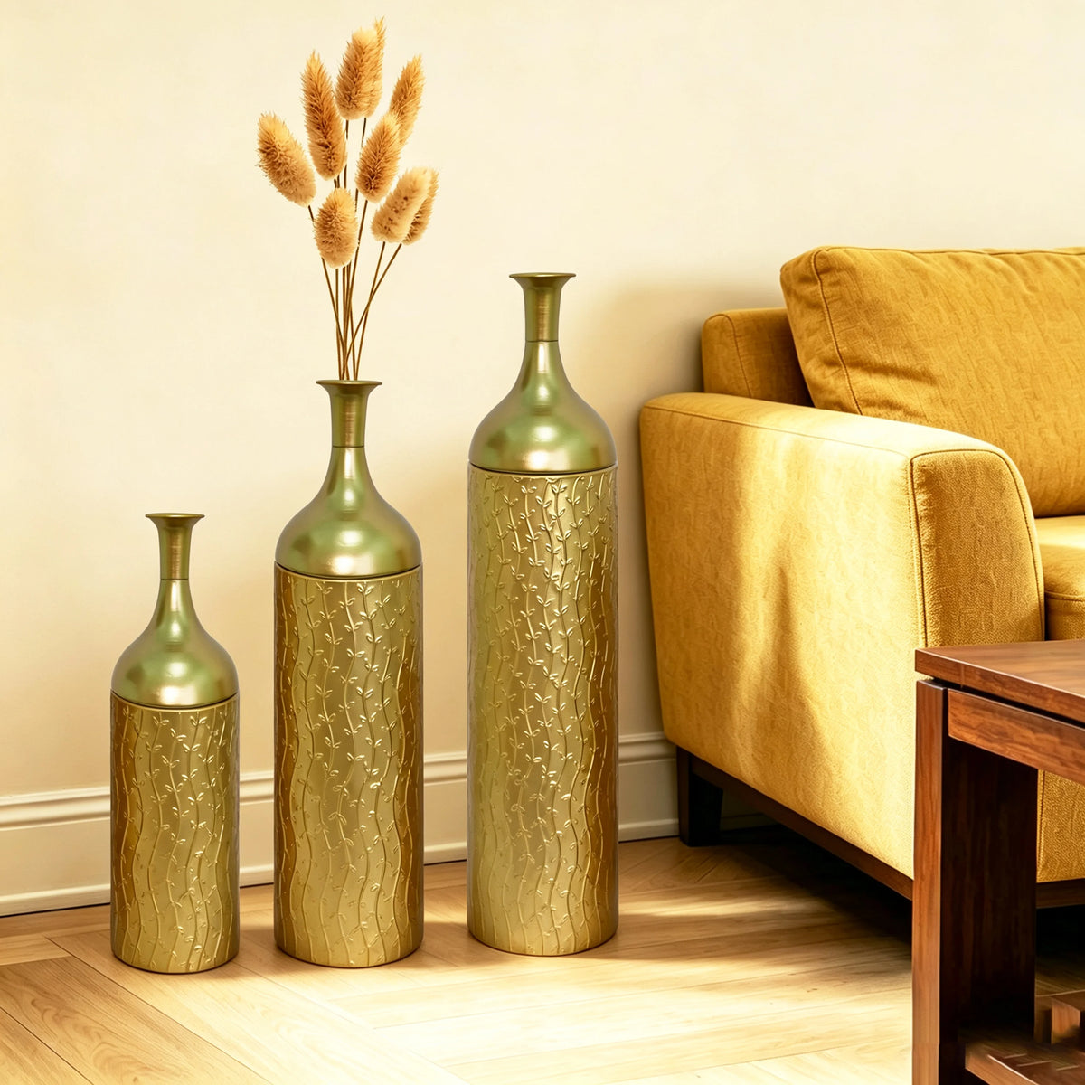 Set of three gold leaf-pattern metal floor vases beside a sofa