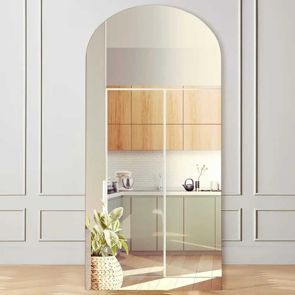 Large arched floor mirror with a slim pale natural wood frame leaning against a white paneled wall
