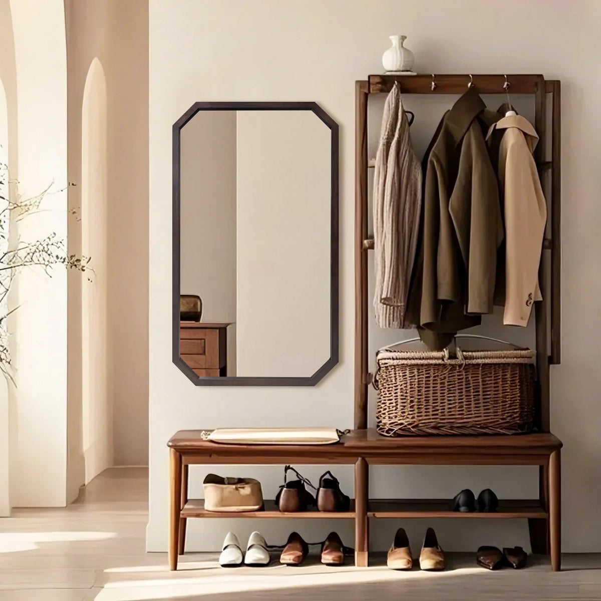 Octagon walnut wood wall mirror hung vertically beside an entryway coat rack and bench