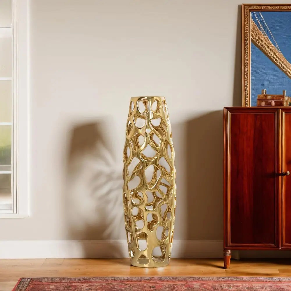 Gold openwork floor vase standing on a rug by a wooden cabinet