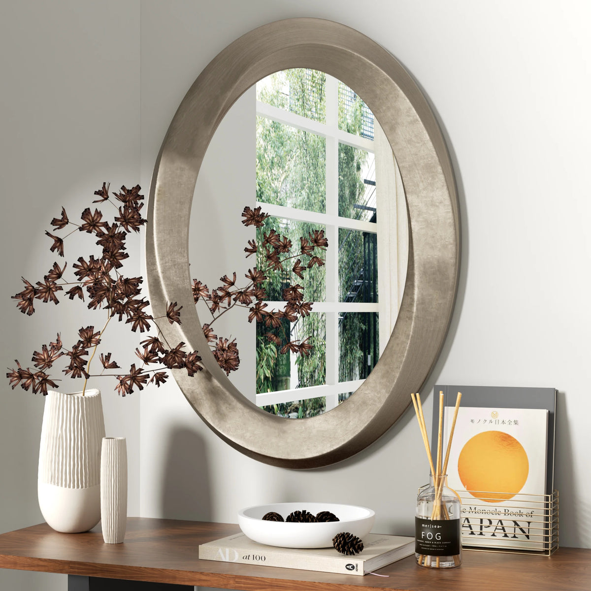 Oval champagne-bronze mirror over a dresser with branches and books