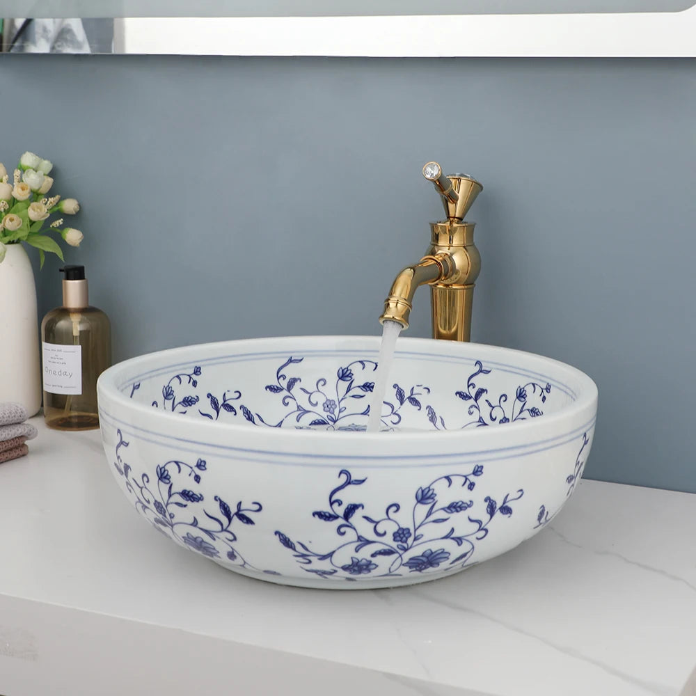 Blue and white floral ceramic vessel sink with gold faucet on a white vanity, side view