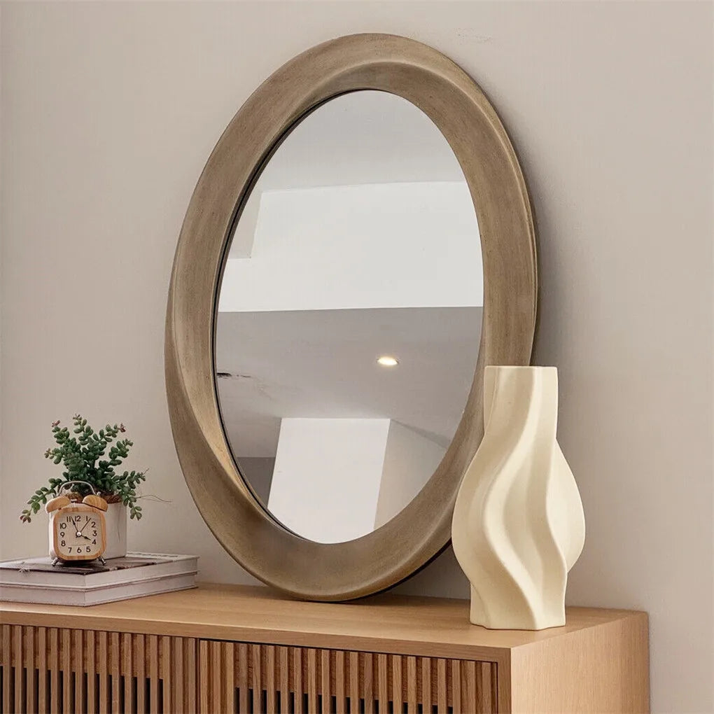 Large oval champagne-finish wall mirror above a wood console with a sculptural vase