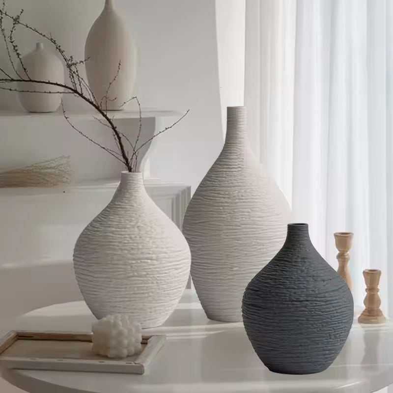 Beige and grey textured ceramic bud vases with dried branches on a counter
