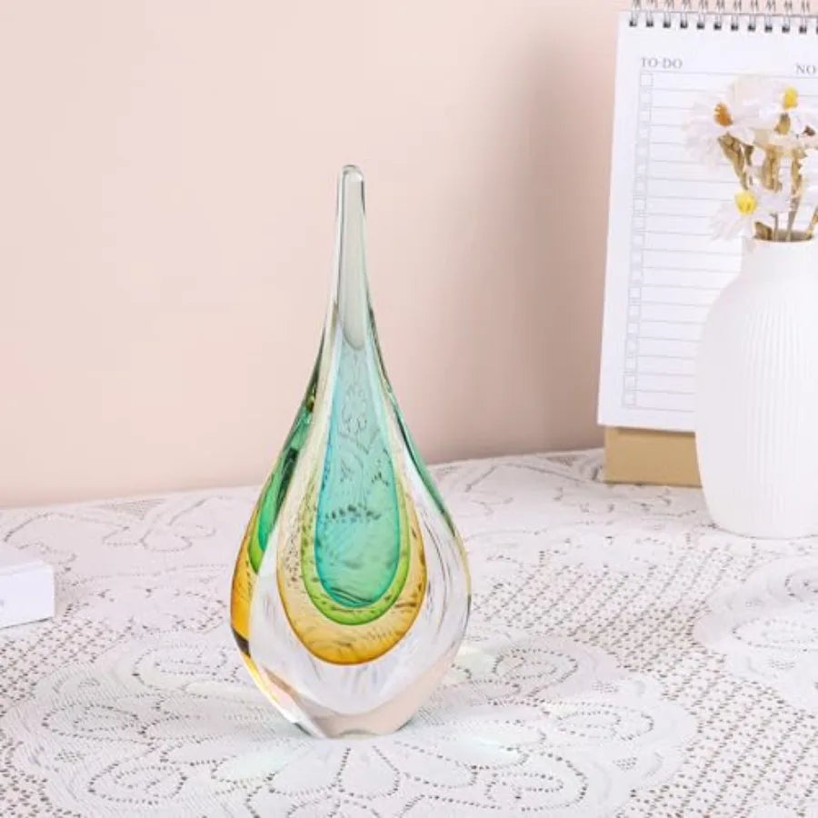 Hand-blown clear glass teardrop sculpture with aqua and amber layers on a lace table runner