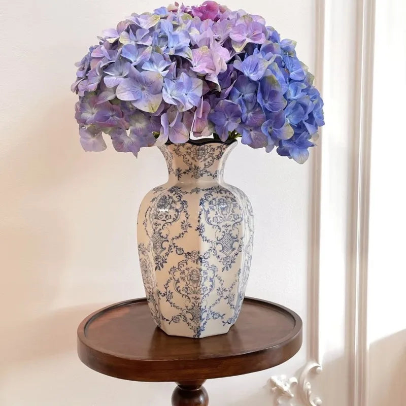 Blue and white porcelain vase with a scalloped rim, filled with purple hydrangeas on a round wooden side table