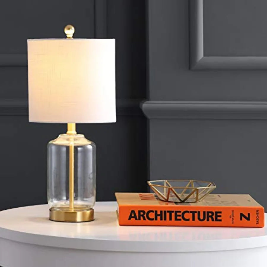 Clear glass and brass table lamp glowing on a white side table beside books