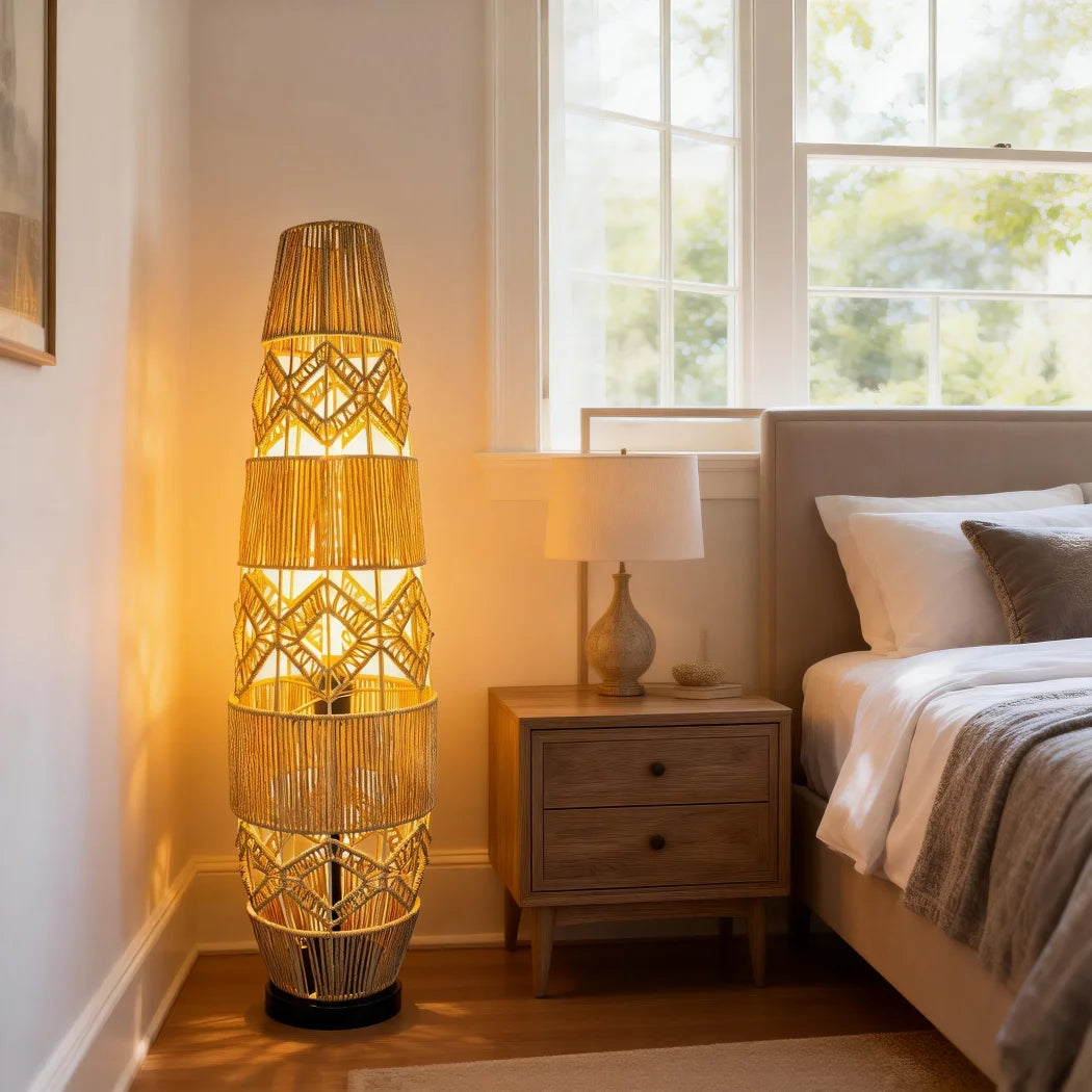 Tall woven cane rattan floor lamp glowing beside a bed