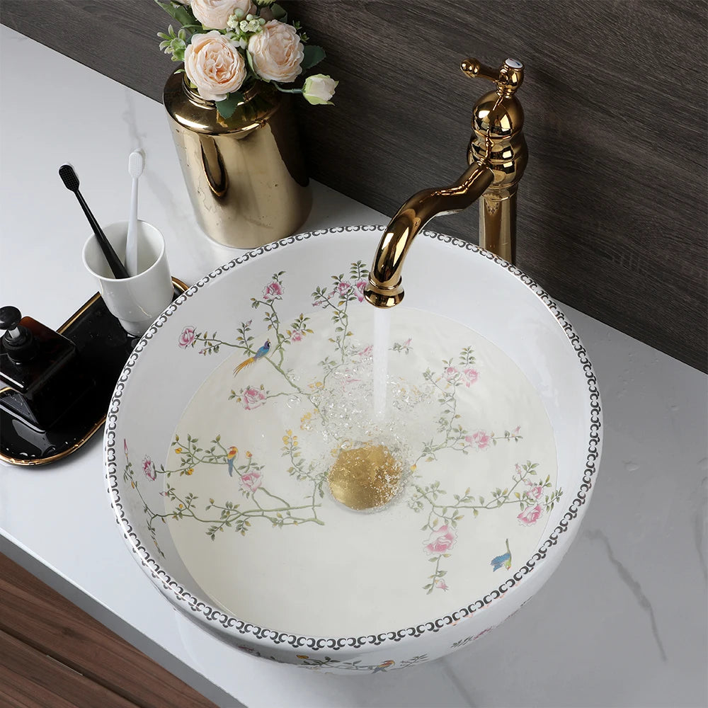 Round white porcelain vessel sink with flower-and-bird pattern and gold faucet
