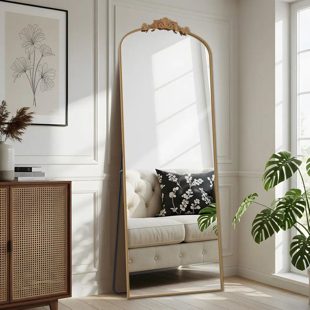 Ornate carved floor mirror with slim gold frame leaning beside a rattan cabinet