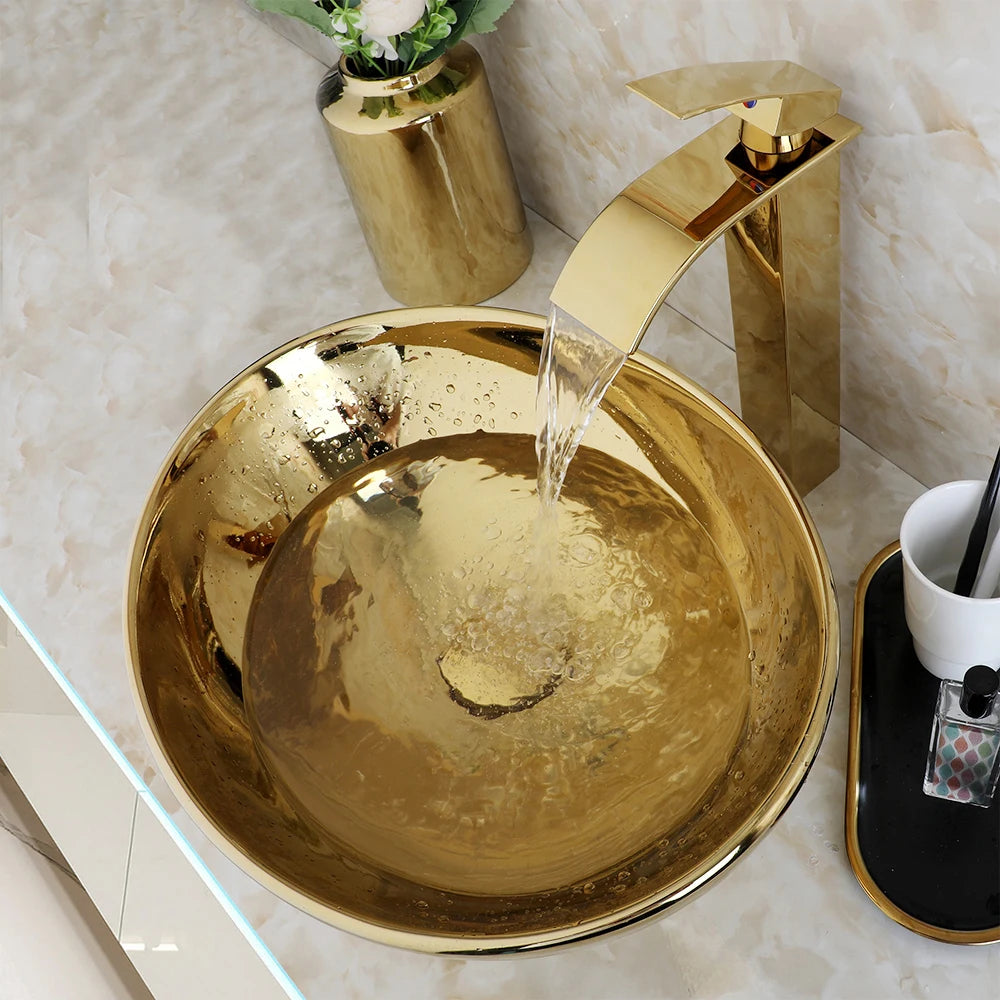 Gold waterfall faucet pouring into the polished gold ceramic round vessel sink