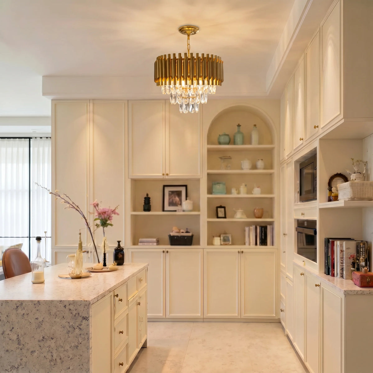 Gold fluted crown crystal chandelier above a kitchen island with cream built-in cabinetry
