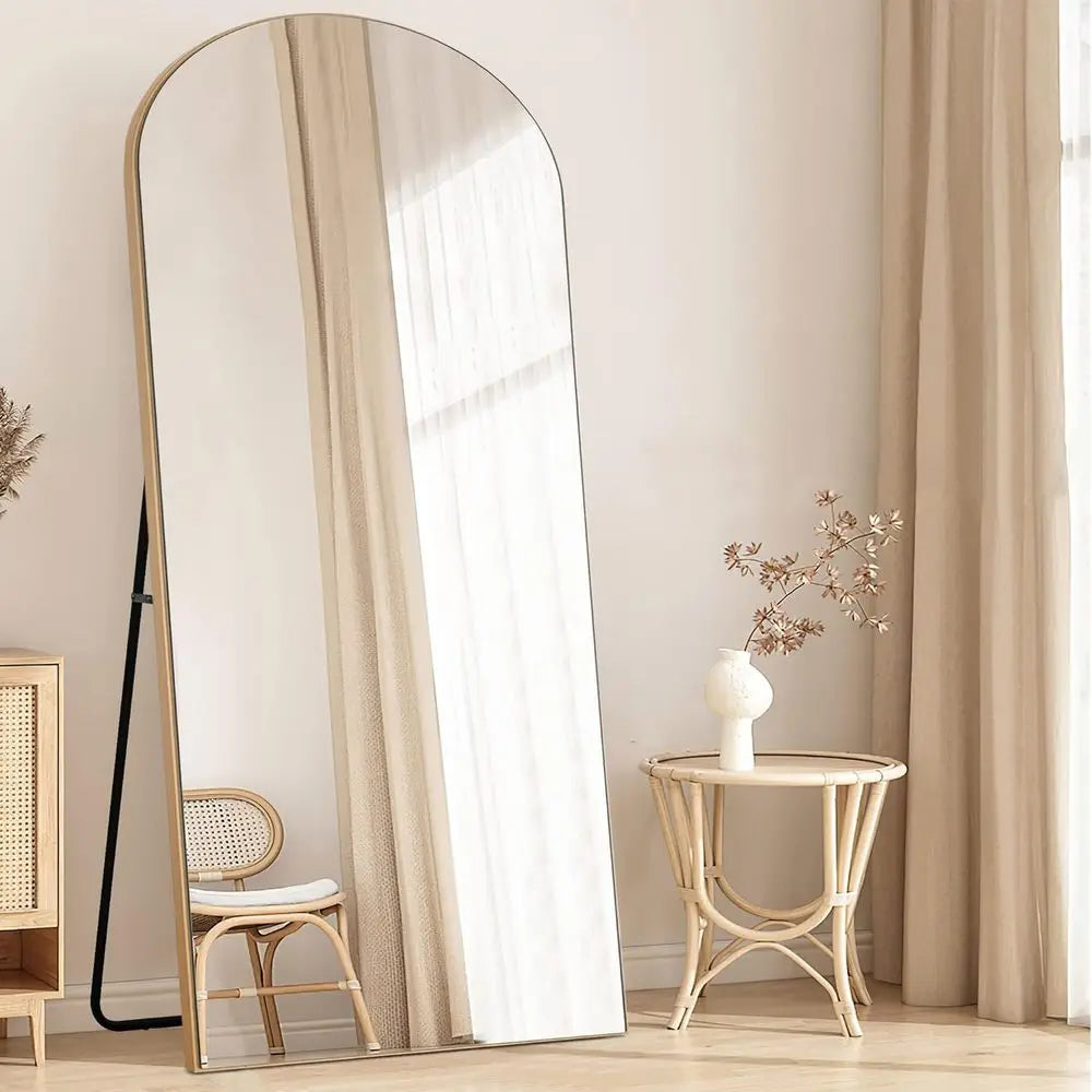 Arched floor mirror with natural wood frame leaning in a bedroom corner