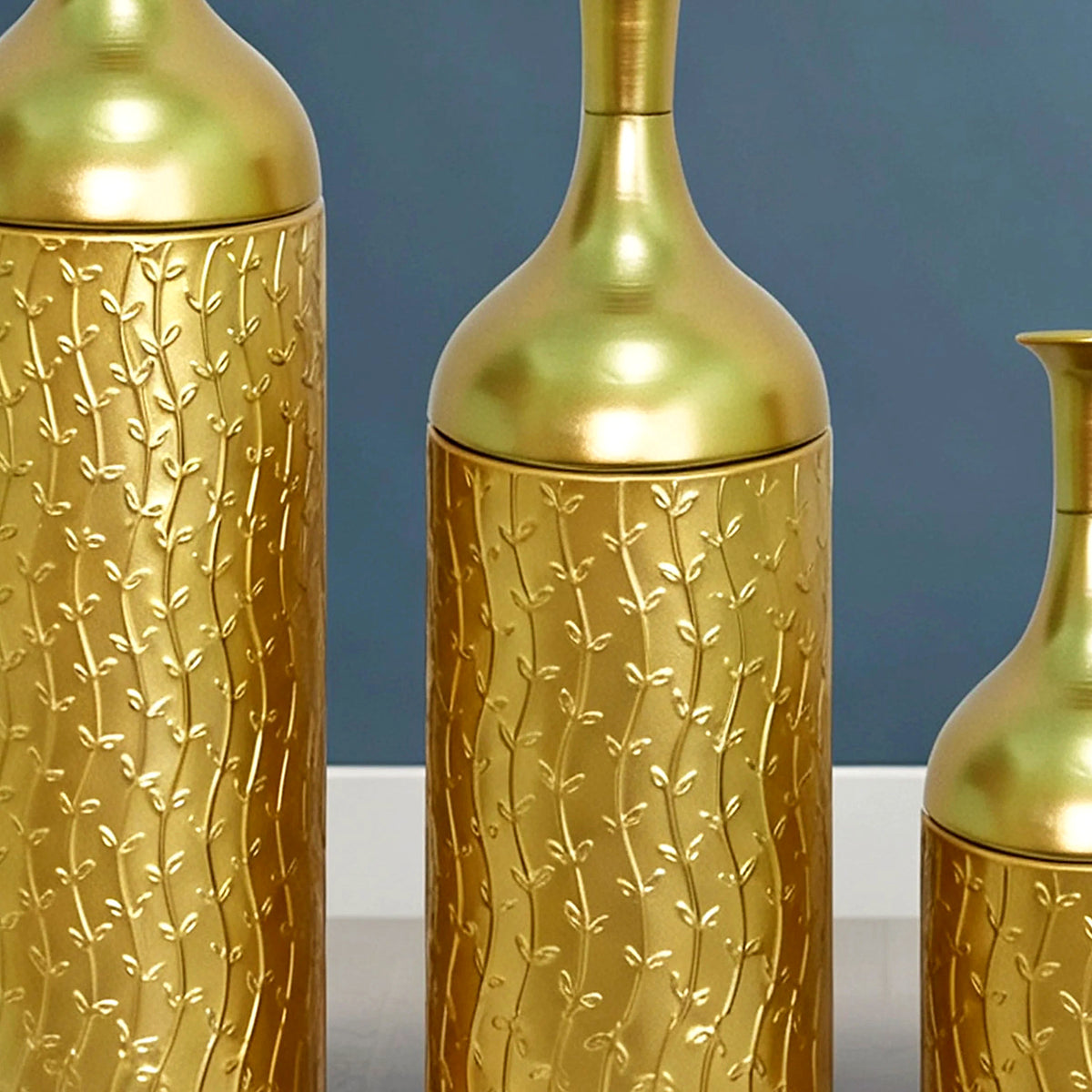Close-up of the embossed leaf texture on the gold metal vase bodies