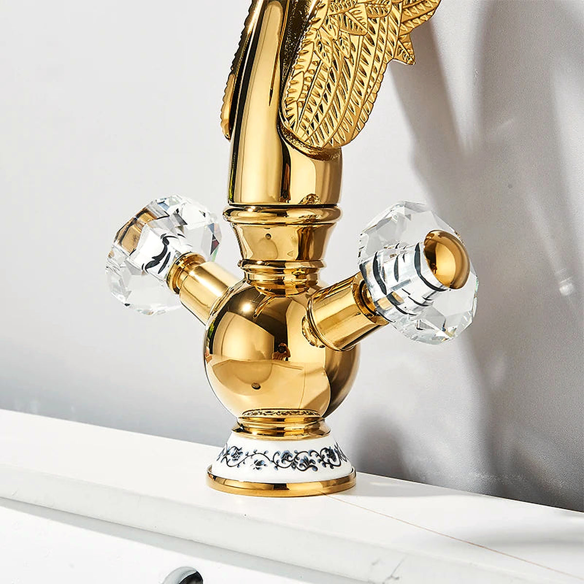 Gold swan-neck basin faucet with faceted crystal cross handles and a blue-and-white porcelain collar on a white vanity