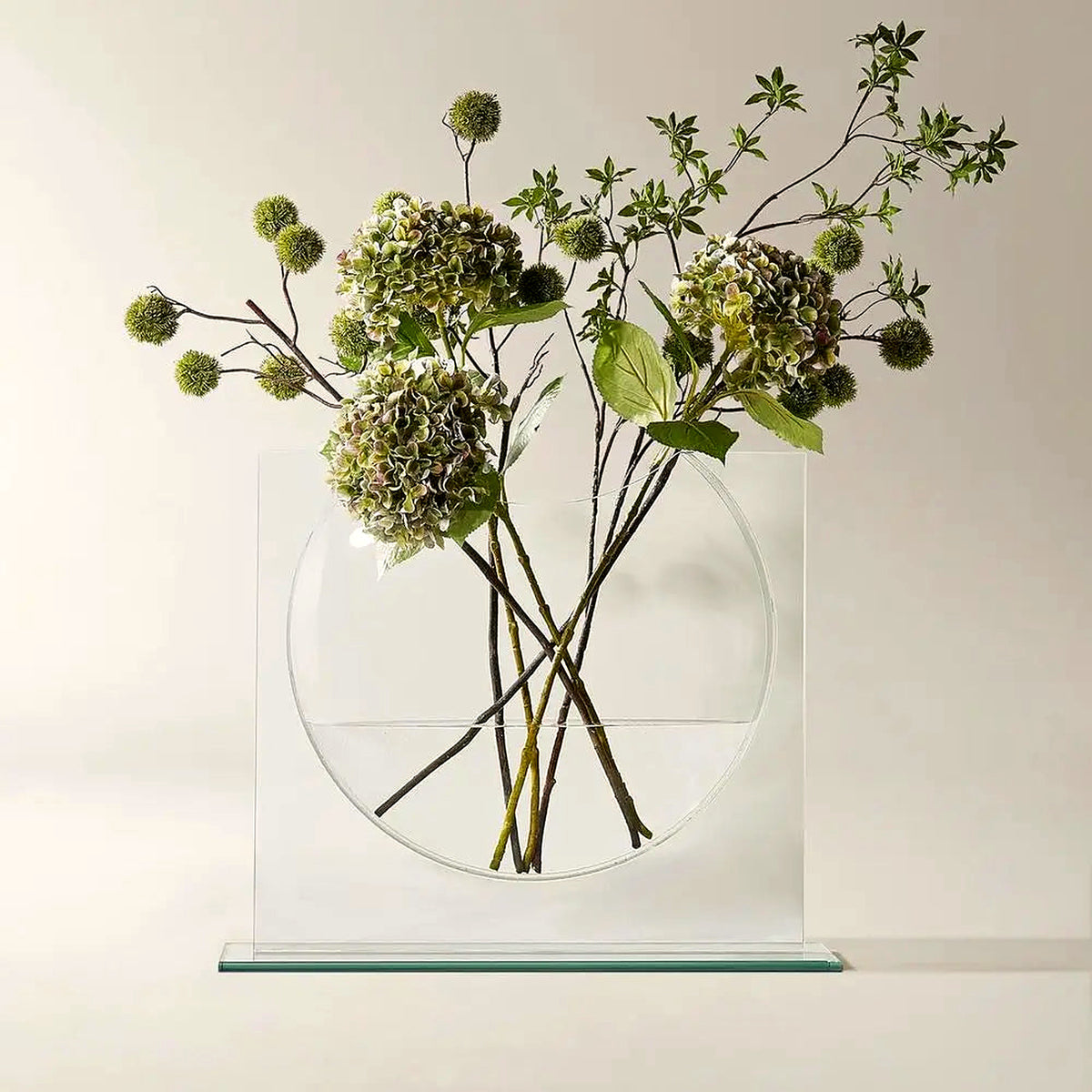 Clear glass ellipse vase in a rectangular glass frame with green hydrangea stems (stems shown for styling)