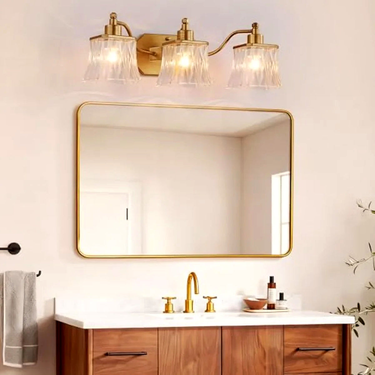 Gold three-light vanity light with ribbed crystal shades above a gold-framed bathroom mirror