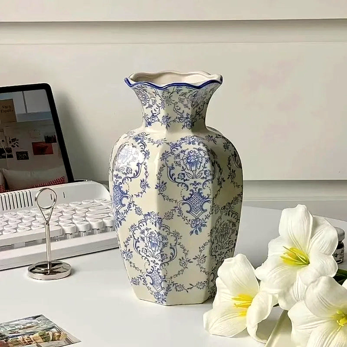 Paneled blue and white porcelain vase with a scalloped rim on a white desk beside fresh lilies
