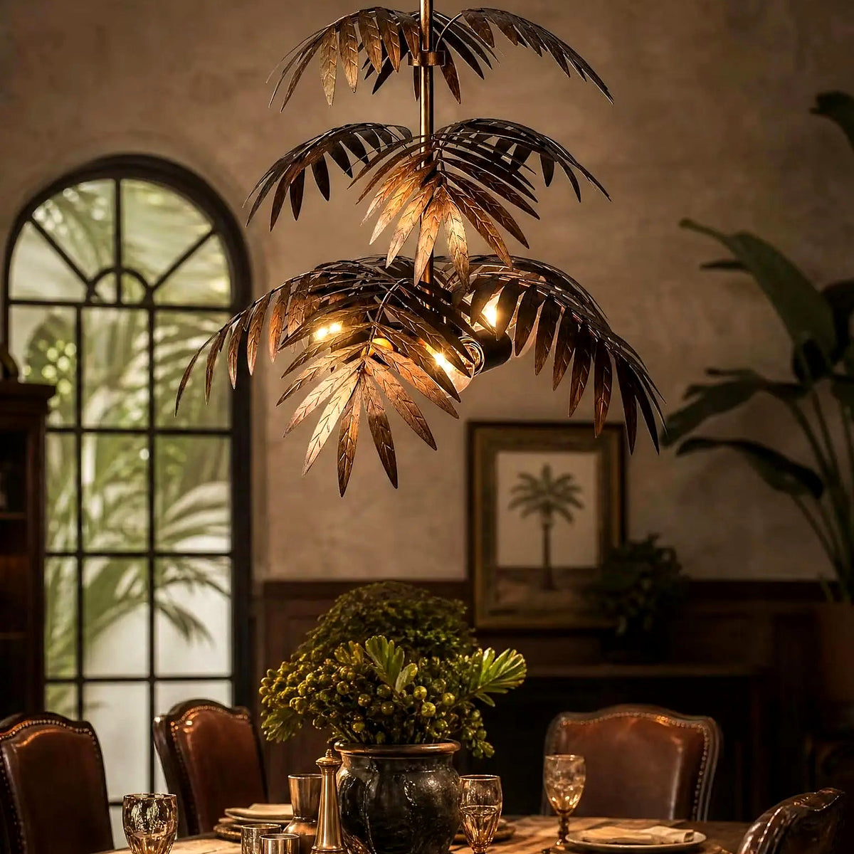 Tiered bronze palm fronds of the pendant chandelier against a textured wall with palm artwork (art shown for styling)