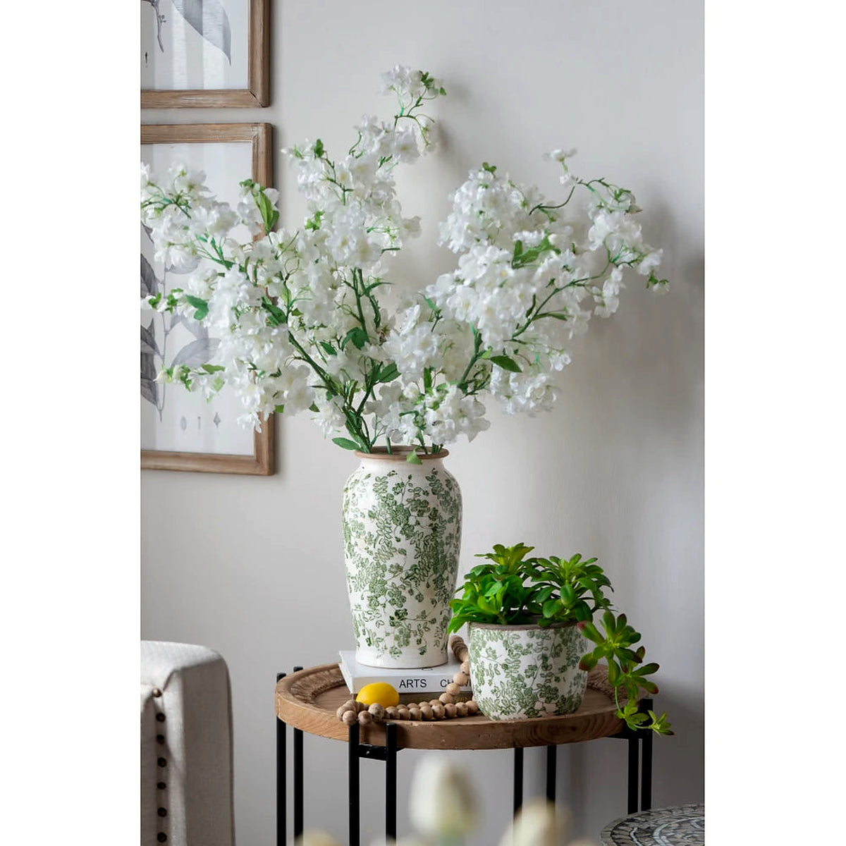 White and green floral ceramic vase with white blooms on a side table (flowers, small planter and décor shown for styling)