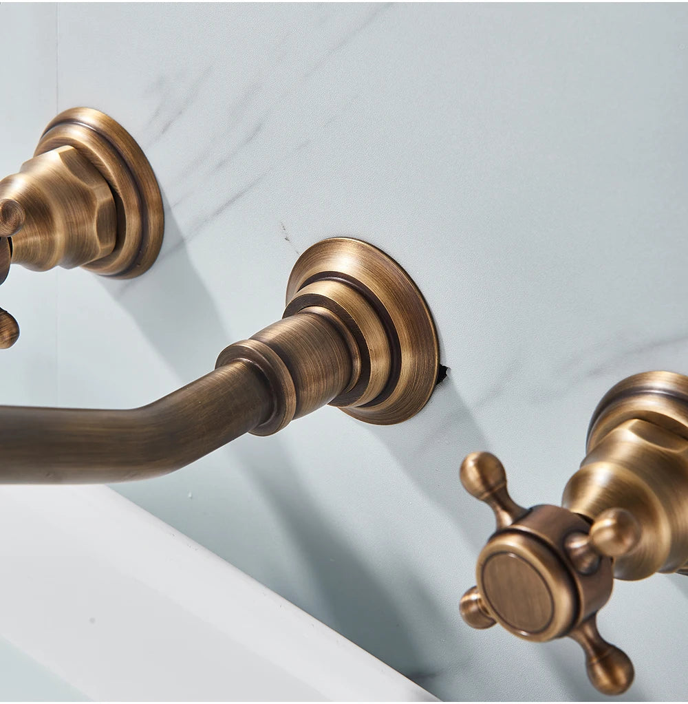 Close-up of the antique brass wall-mount spout and cross handle against white marble