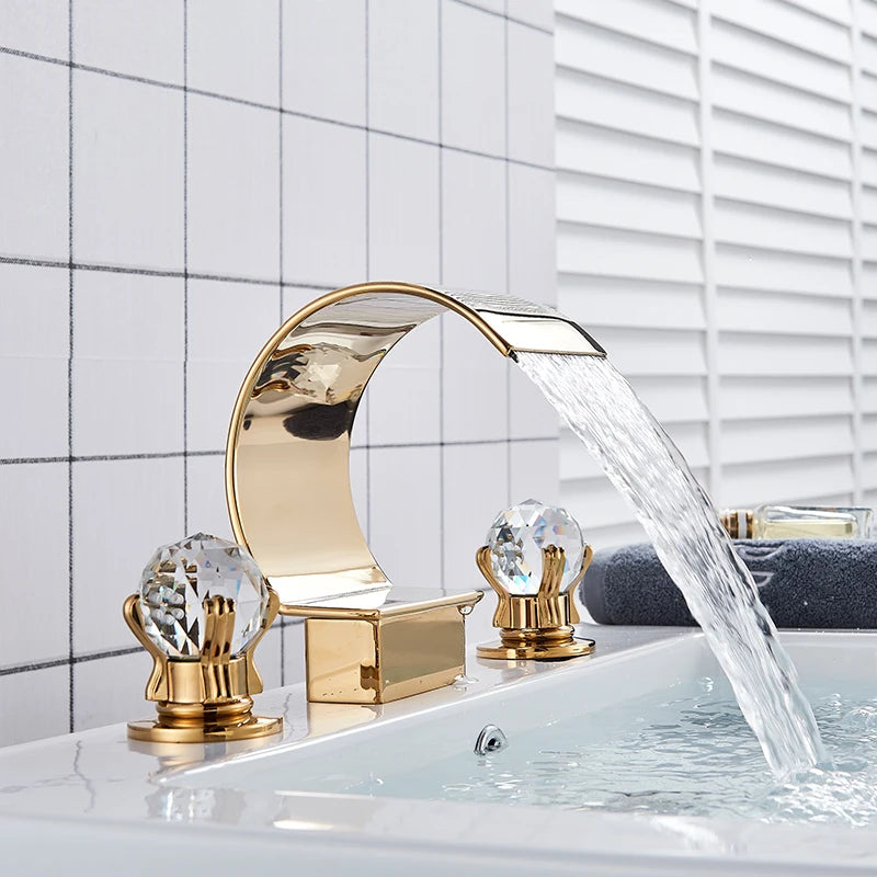 Angled view of the gold waterfall widespread faucet with faceted crystal-style knob handles