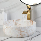 White marble-look vessel sink with gold waterfall faucet under a round mirror