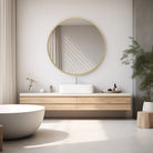 Round matte gold frame mirror above a floating wood vanity with a vessel sink