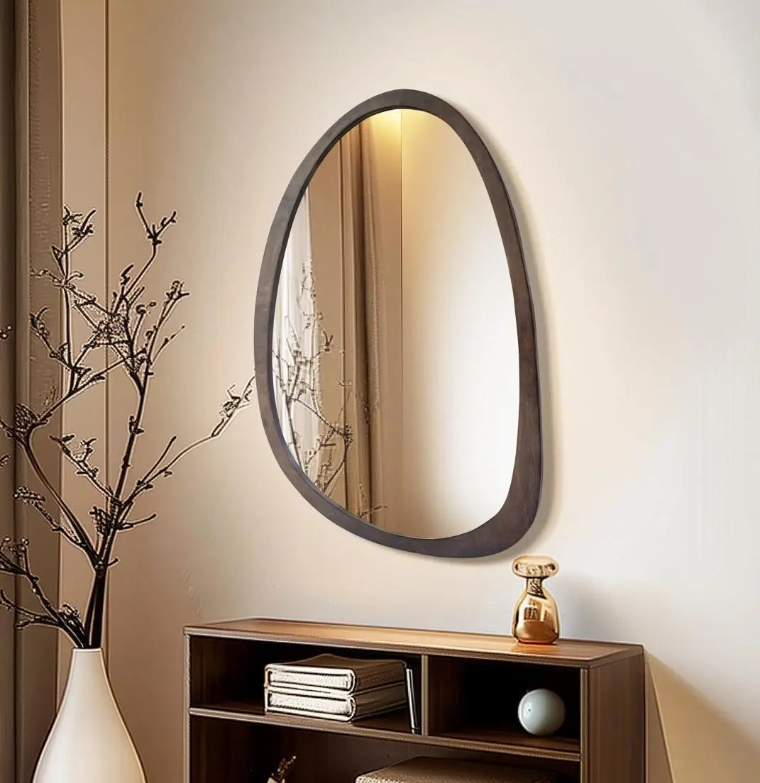 Organic irregular walnut wood wall mirror above a low console with branches and vase