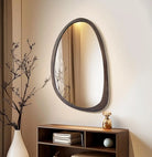 Organic irregular walnut wood wall mirror above a low console with branches and vase