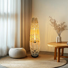 Tall cane floor lamp next to a pouf and side table