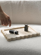 Scalloped travertine tray on a white bench with lipstick and perfume