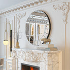 Venetian-style round mirror with segmented mirrored border hung above a carved marble fireplace