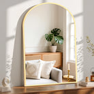 Arched gold metal frame mirror leaning on a console in a sunlit living room