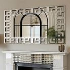 Greek-key Venetian mirrored glass wall mirror hung horizontally above a mirrored fireplace mantel