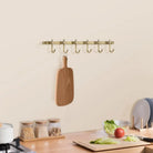 Brushed brass towel rail with six curved hooks (mounted in a kitchen)