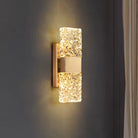 Pair of textured ripple glass LED wall sconces with gold frame glowing on a dark wall