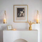 Two gold candle wall sconces flanking a framed print above a white console