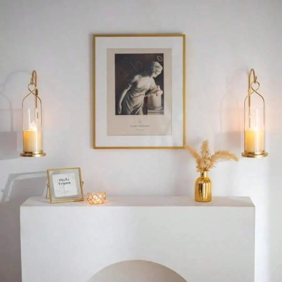 Two gold candle wall sconces flanking a framed print above a white console