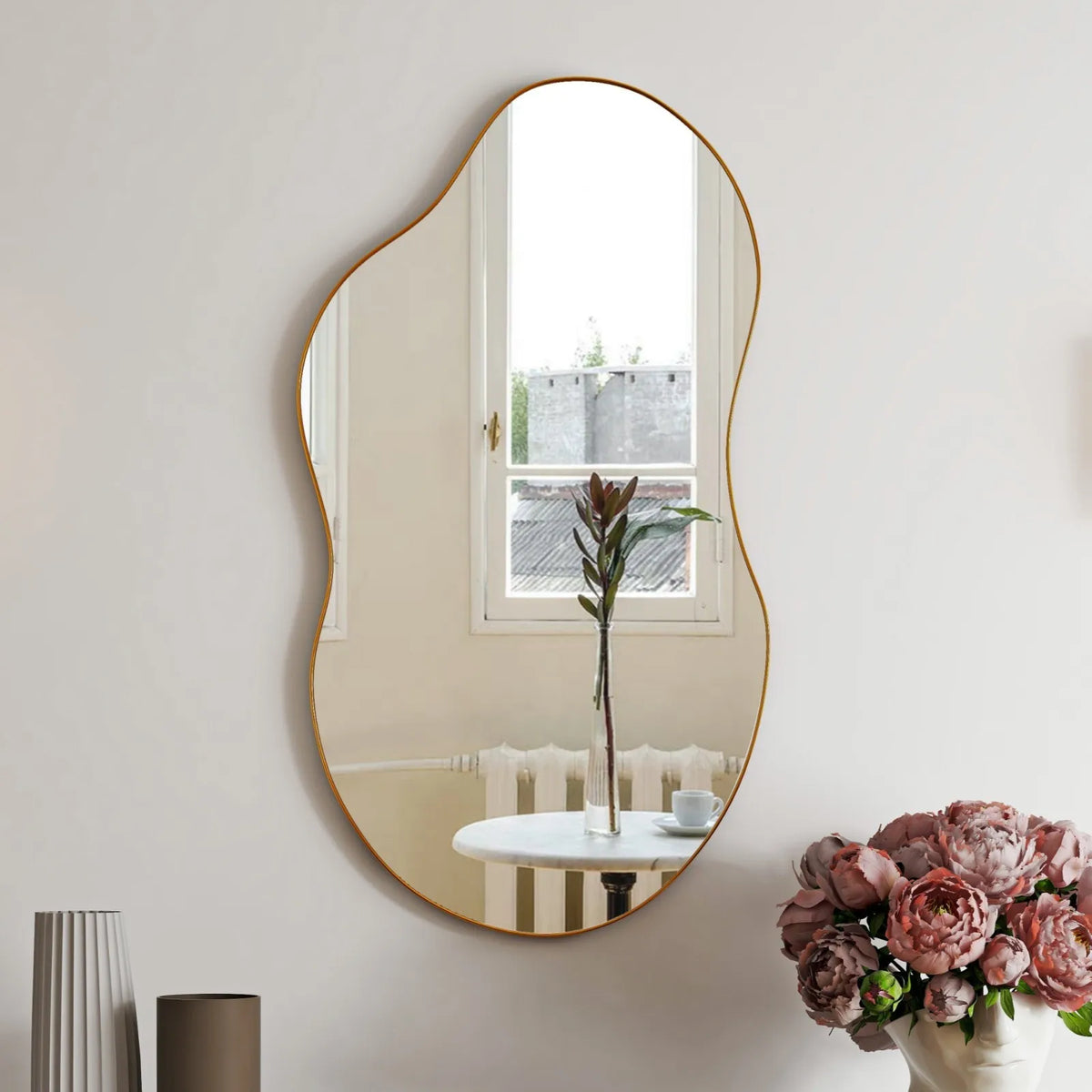 Gold wavy asymmetrical wall mirror hung vertically above pink flowers