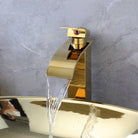 Close-up of the gold waterfall faucet over the gold oval basin