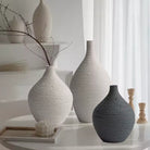Beige and grey textured ceramic bud vases with dried branches on a counter