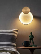 Round marble-look LED wall sconce with brass disc glowing on a dark wall