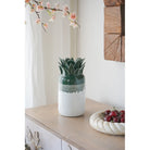 Green and white ombre ceramic pineapple vase on a white console beside a fruit bowl