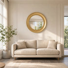 Brushed gold round mirror above a cream sofa