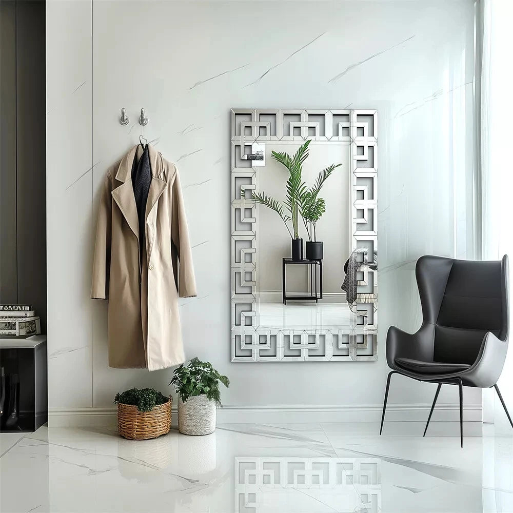 Greek-key Venetian wall mirror hung vertically in a white entryway beside a coat hook