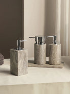 Square and round gray travertine soap dispensers with silver-tone pumps on a slim tray