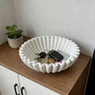 White pleated ceramic bowl with a scalloped rim on a coffee table